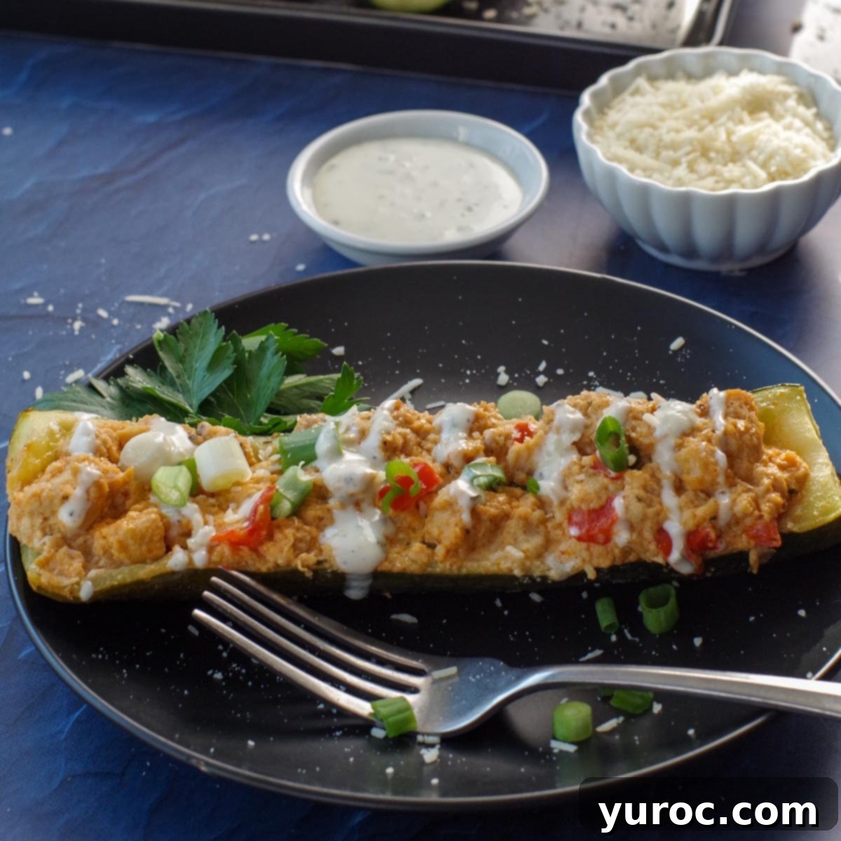 buffalo chicken zucchini boats with ranch dip and parmesan cheese in white bowls in the background