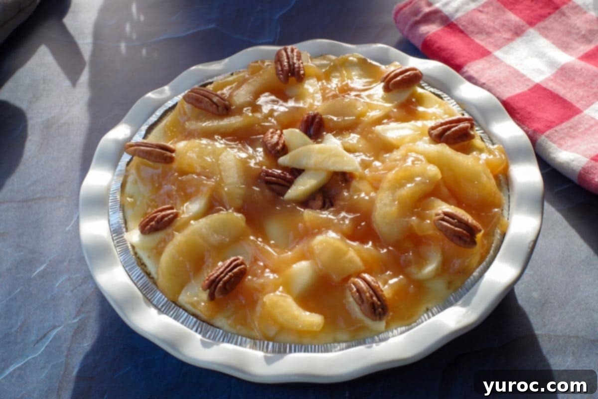 The finished caramel apple cheesecake pie, garnished with pecan halves arranged on apple slices and chopped pecans sprinkled in the center, ready to be chilled.