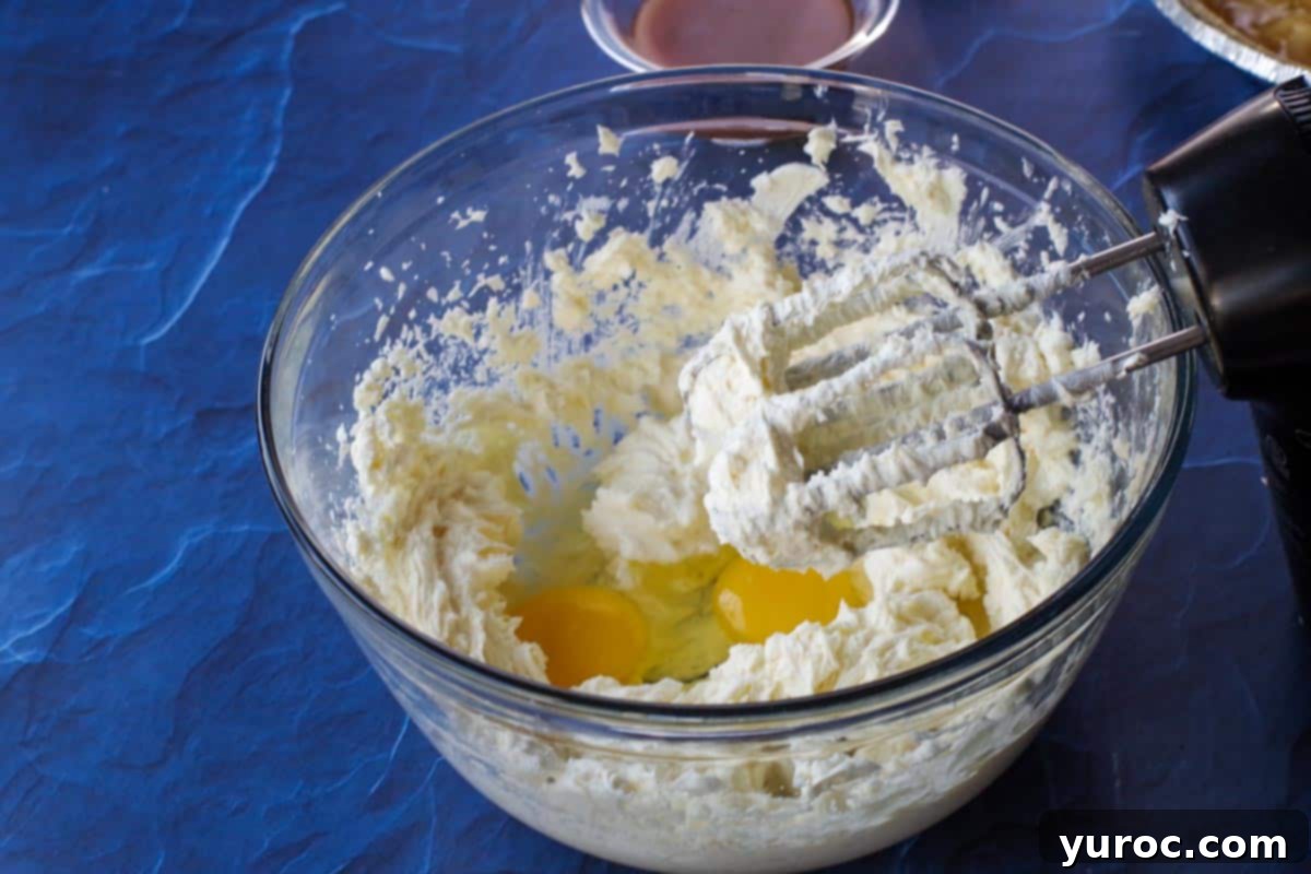 Eggs being added to the creamy cream cheese mixture in a large glass bowl, ready for final mixing.