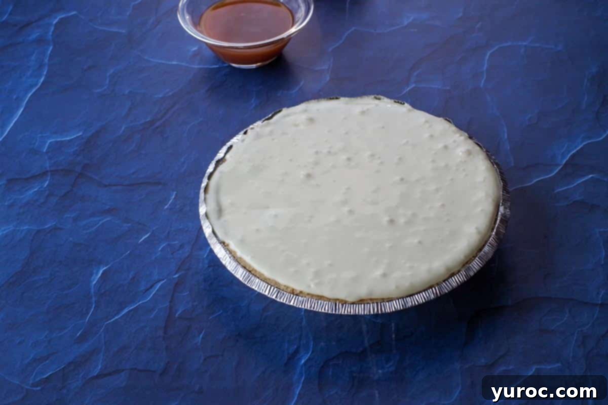 Smooth cheesecake batter being carefully poured into the pie shell, over the layer of apple pie filling.