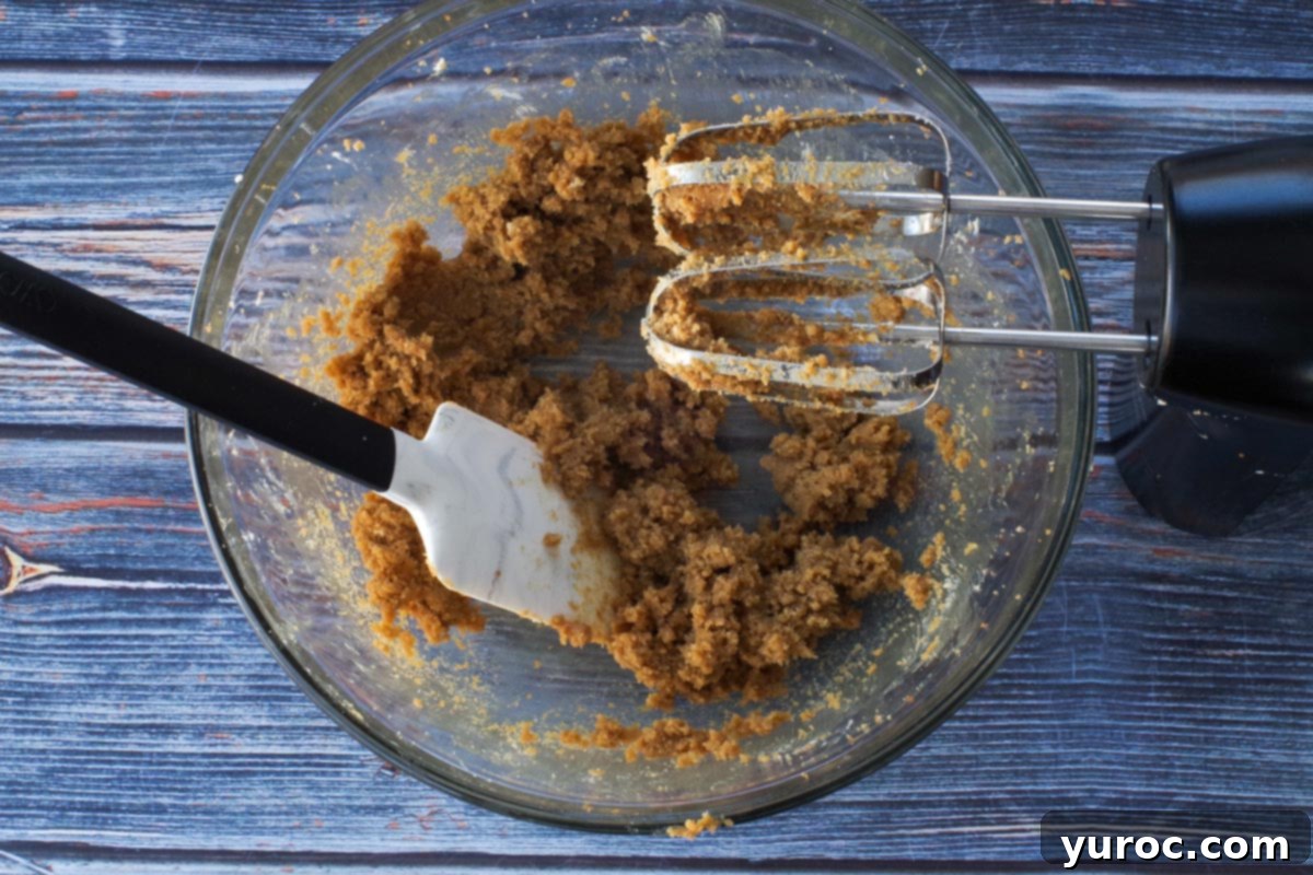 Butter and brown sugar creamed together in a large glass bowl with a spatula in it and and an electric mixer beaters over top.