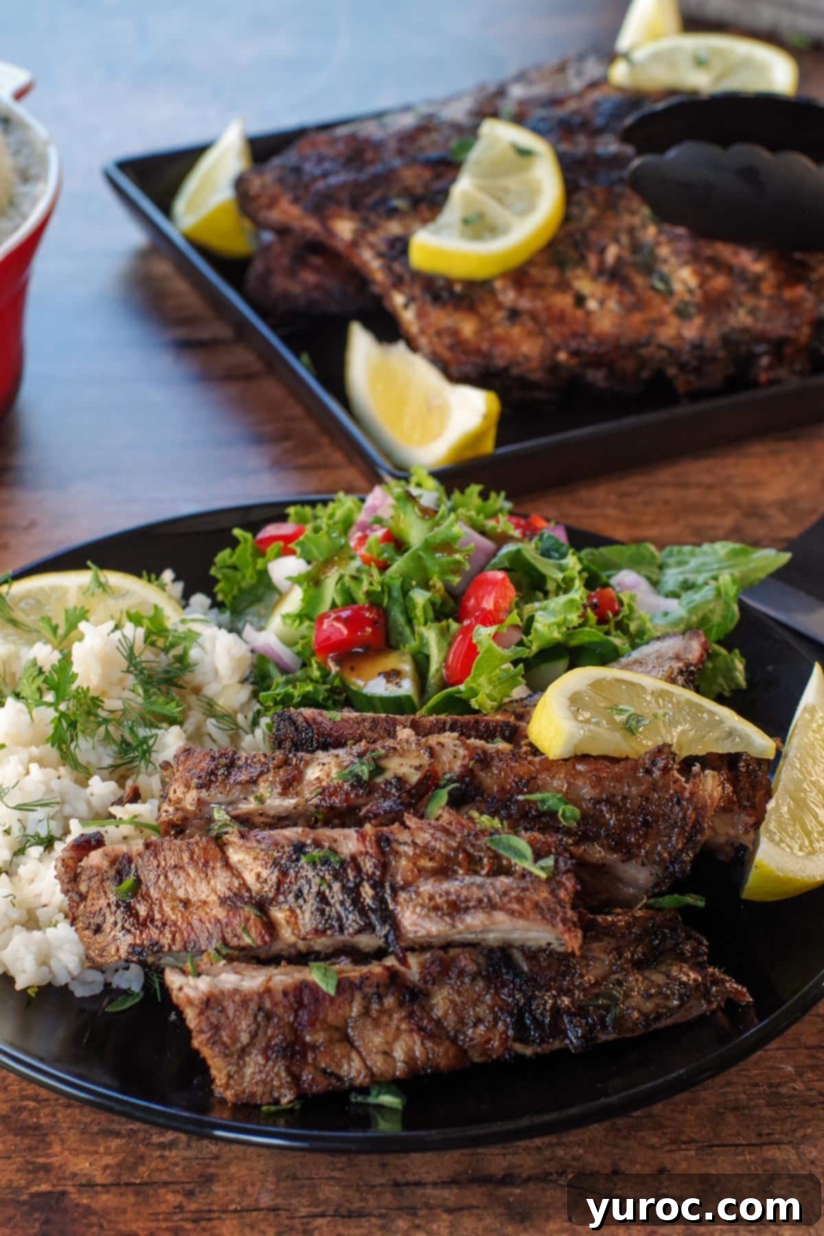 Cut Greek ribs on a plate with Greek rice and salad, with tray of ribs in the background