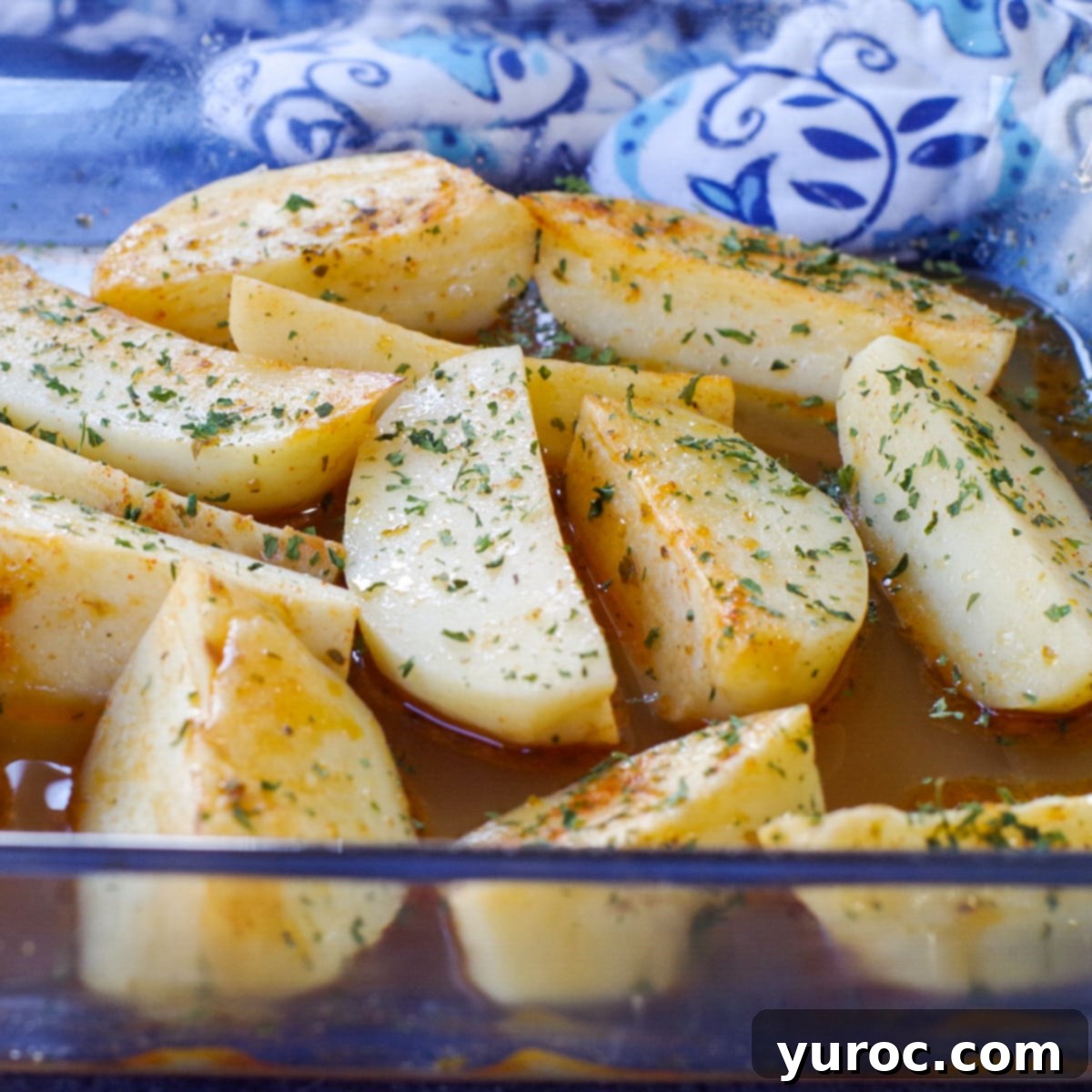 Greek potatoes in a glass pan with a blue patterned oven mitt in the background
