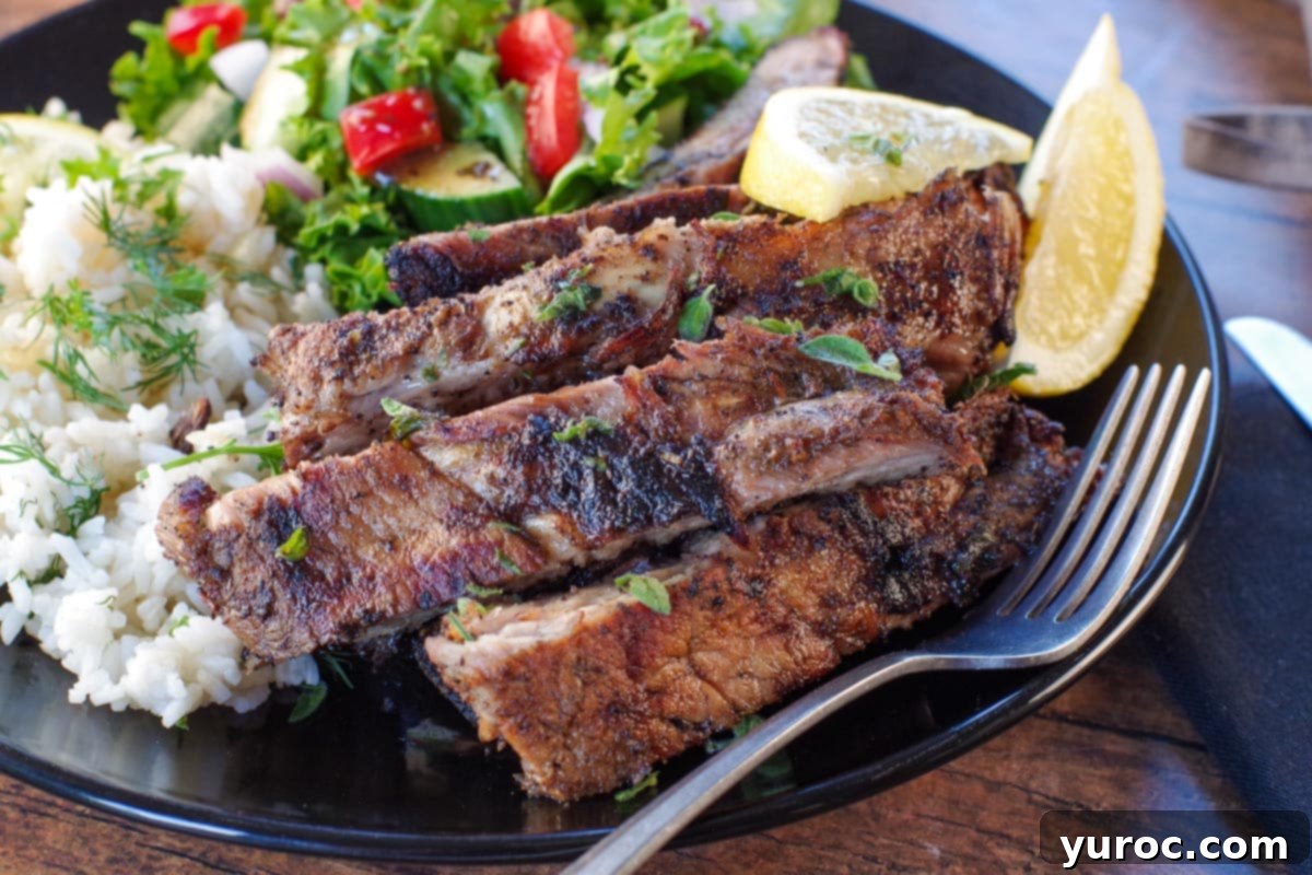 Cut Greek ribs on a plate with Greek rice and salad, with fork on plate