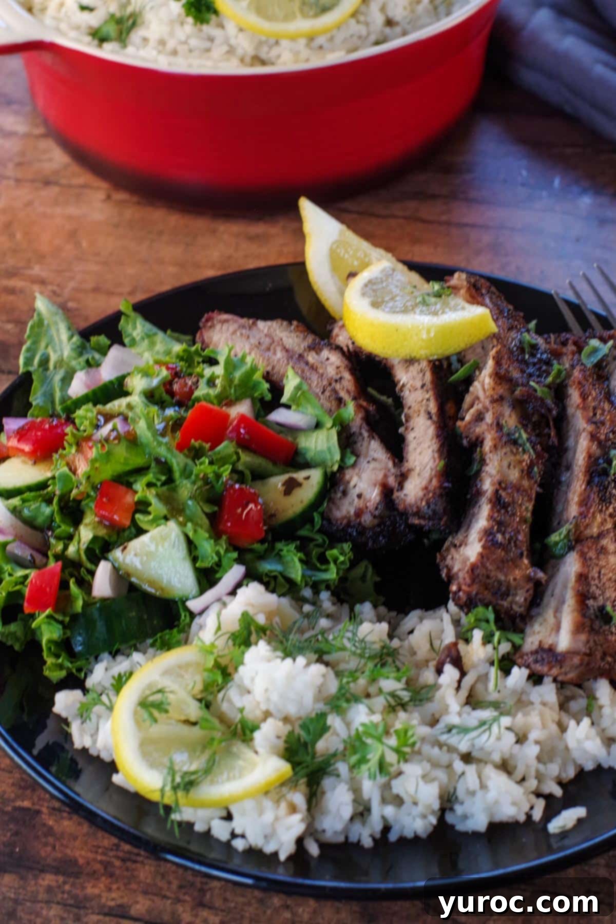 eek rice with Greek ribs and salad on a black plate.