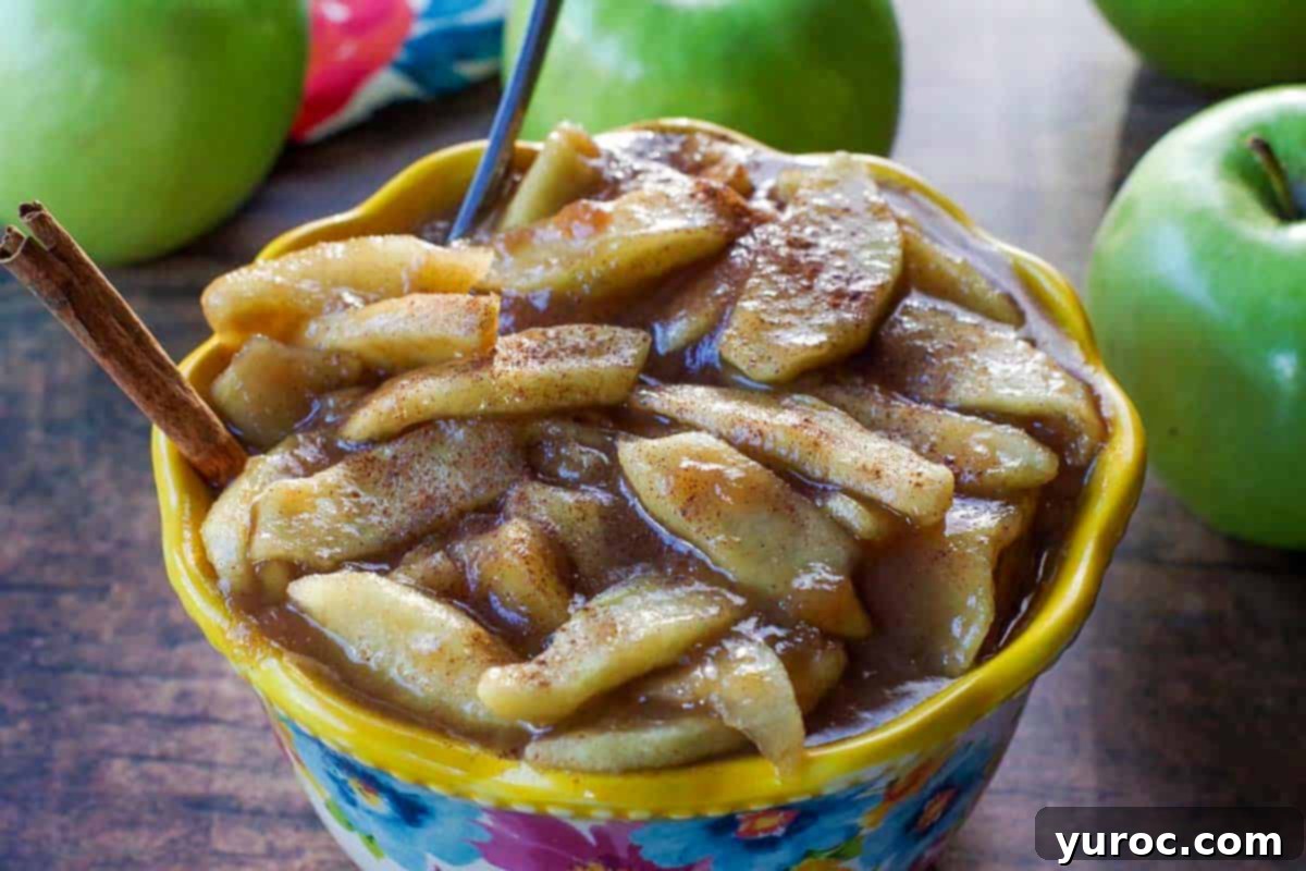 stovetop apple pie filling in a flowered blue bowl with yellow rim, with spoon and cinnamon stick in it