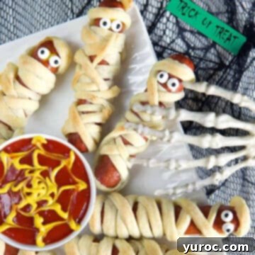 mummy hot dogs on white plate with ketchup in white bowl with spider web