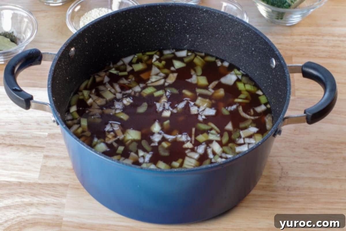 Wholesome Minestrone Made Easy 3 A blue soup pot simmering with a rich broth, diced tomatoes, finely chopped garlic, celery, and onion, creating the aromatic base for minestrone.