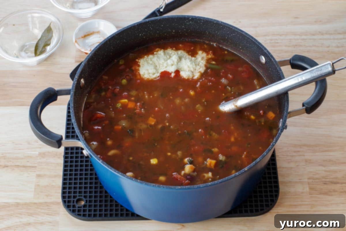 Wholesome Minestrone Made Easy 5 A bowl of minestrone soup, freshly seasoned with grated Parmesan cheese and a swirl of sriracha sauce, ready for serving.
