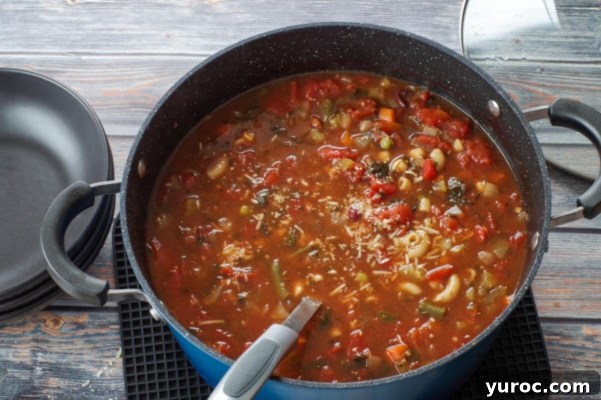 Wholesome Minestrone Made Easy 6 A blue pot of minestrone soup with a ladle, ready to be served into black bowls on the left, with the glass lid to the right.