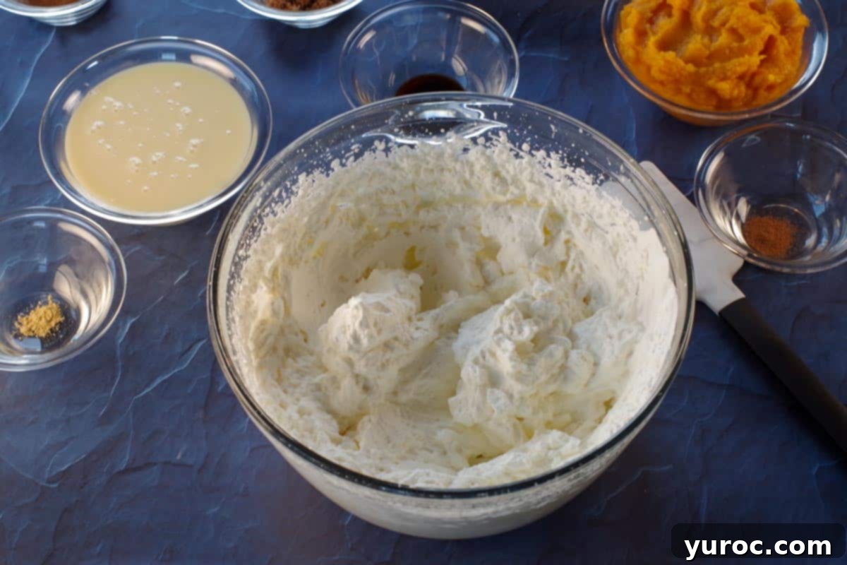 Heavy whipping cream being beaten in a large bowl with an electric mixer until stiff peaks form.
