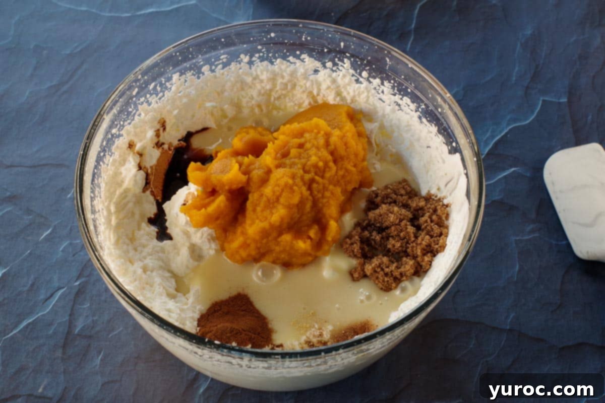 All pumpkin pie ice cream ingredients (whipped cream, pumpkin puree, condensed milk, spices, and brown sugar) combined in a large glass bowl, ready for mixing.