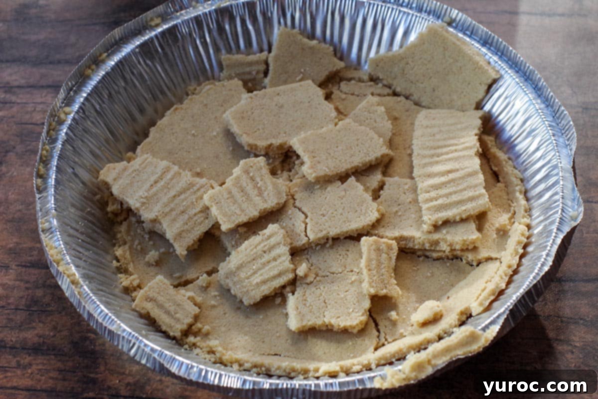 Broken pieces of graham cracker crust in an aluminum pie plate, ready to be used as a topping for the pumpkin ice cream.