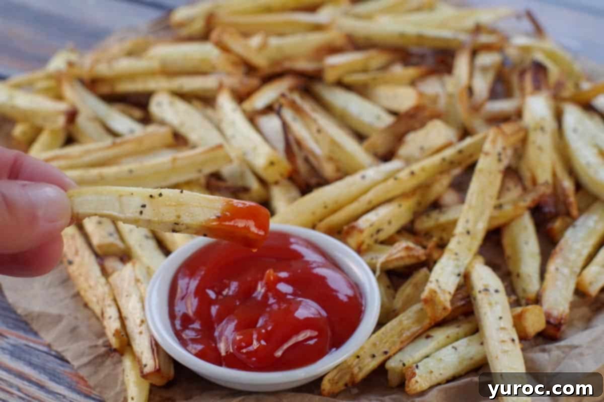 Crispy parsnip fries artfully arranged on brown paper, with one fry being dipped into a small white bowl of ketchup.