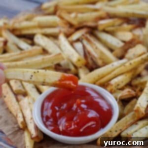 Crispy Parsnip fries on brown paper with one fry being dipped into a white bowl of ketchup