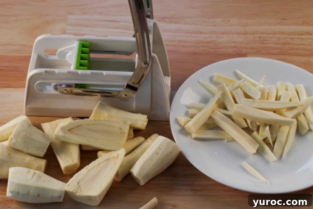 Parsnip roots being uniformly cut into fry shapes using a French fry chipper.