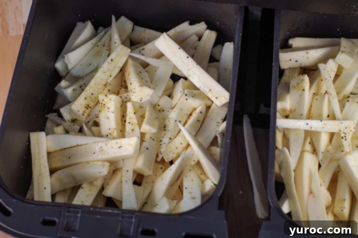 Seasoned parsnip chips in an air fryer drawer, sprinkled with lemon pepper, ready for cooking.