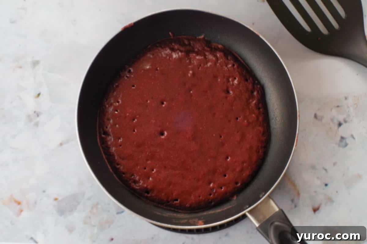 Healthy Red Velvet Pancakes with Luscious Chocolate Cream Cheese Butter 12 Pancakes bubbling in a frying pan, indicating they are ready to be flipped.