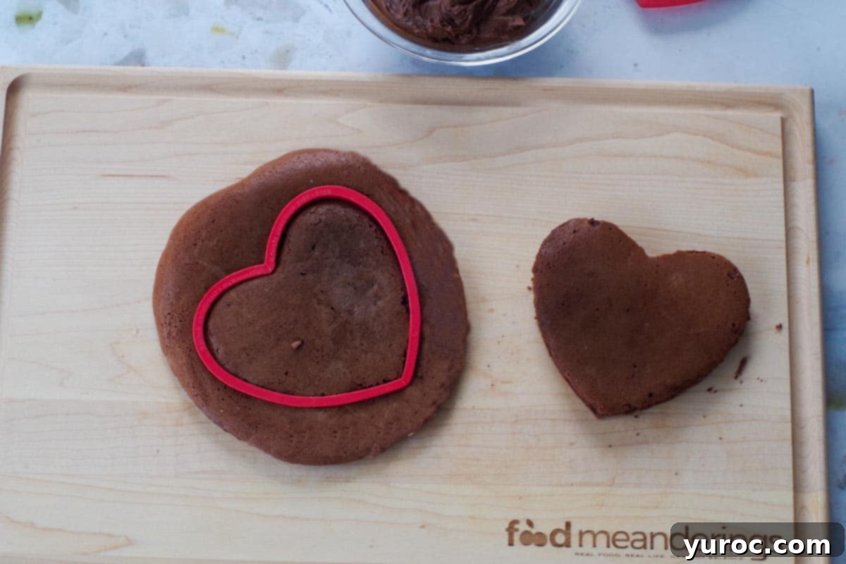 Healthy Red Velvet Pancakes with Luscious Chocolate Cream Cheese Butter 14 A healthy red velvet pancake with a heart-shaped cookie cutter cutting out a shape, and another heart-shaped pancake already cut, on a wooden cutting board.