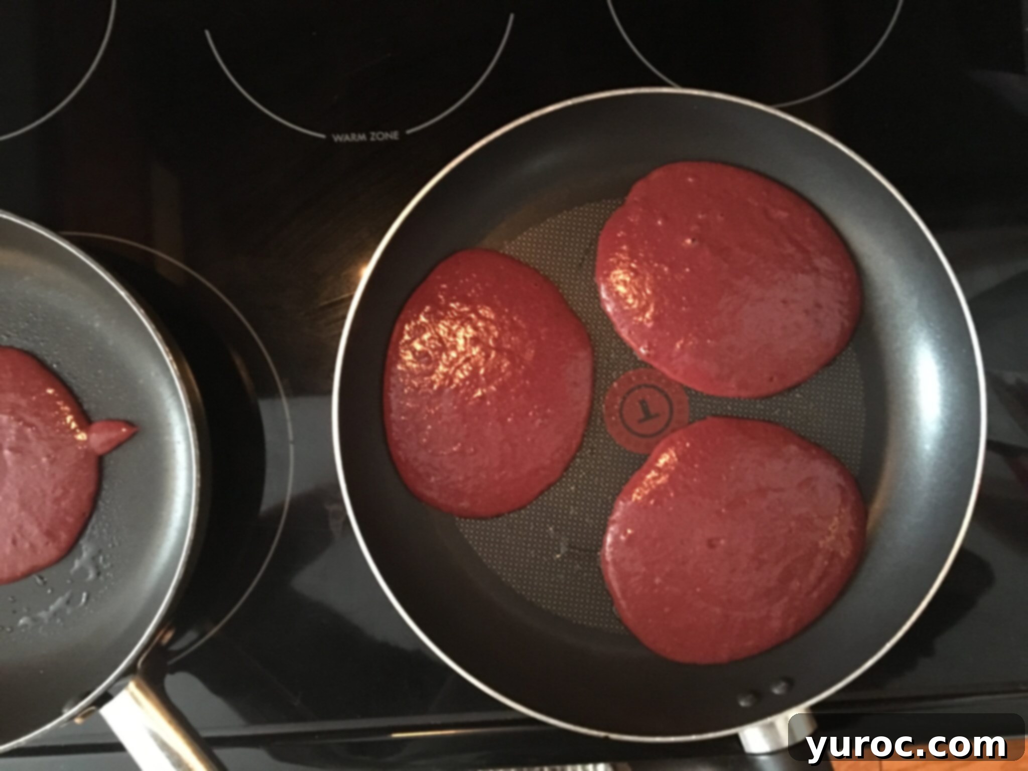 Healthy Red Velvet Pancakes with Luscious Chocolate Cream Cheese Butter 18 Three healthy red velvet pancakes cooking in a large frying pan on a stovetop.