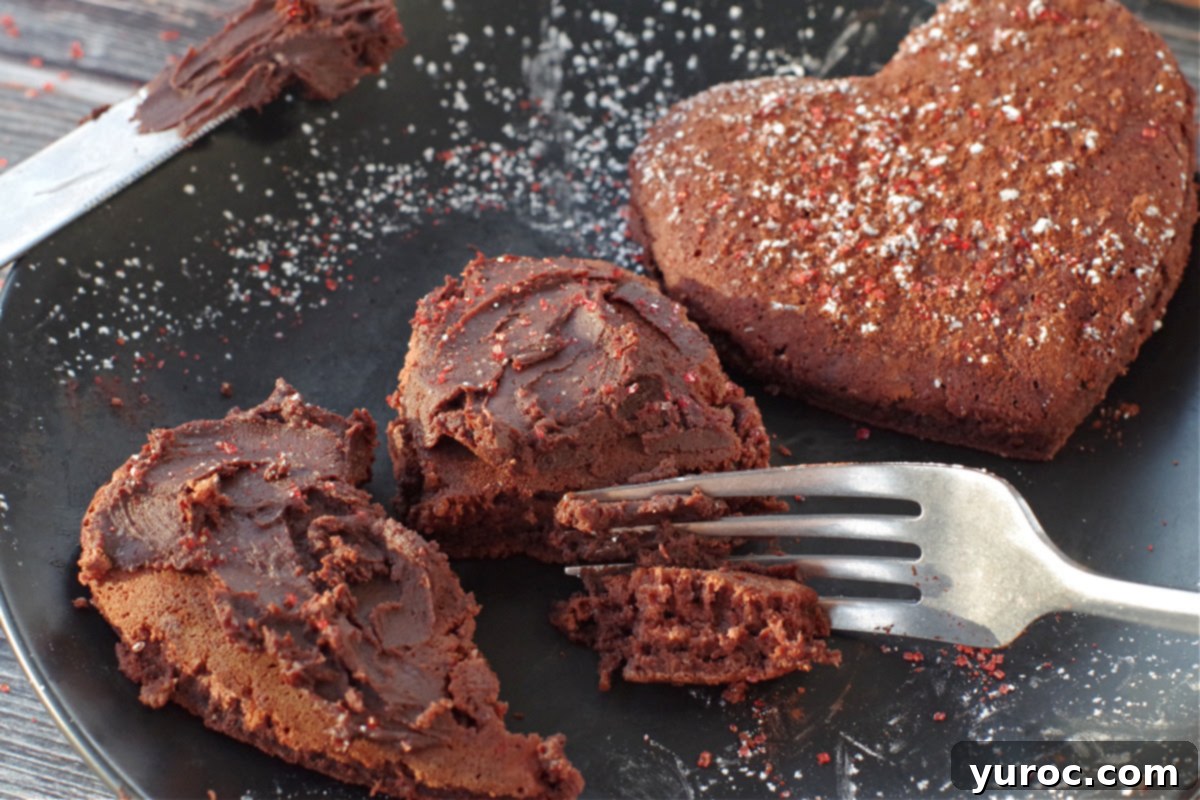 Healthy Red Velvet Pancakes with Luscious Chocolate Cream Cheese Butter 19 Two heart-shaped red velvet pancakes on a black plate, one with chocolate cream cheese butter being cut into, and the other with red sparkling sugar and powdered sugar.