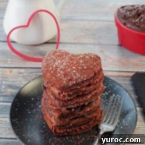 Healthy Red Velvet Pancakes with Luscious Chocolate Cream Cheese Butter 21 Stack of heart-shaped red velvet pancakes on a black plate with a heart cookie cutter in the background.