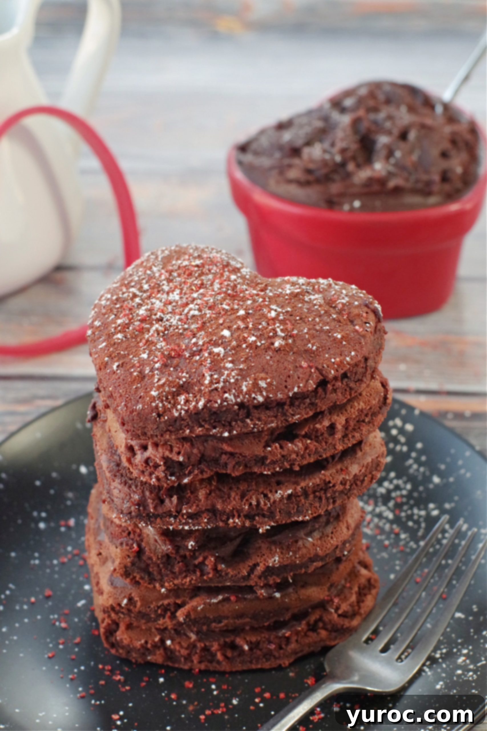 Healthy Red Velvet Pancakes with Luscious Chocolate Cream Cheese Butter 5 Stack of six healthy red velvet pancakes on a black plate with a fork and a heart-shaped dish of chocolate cream cheese butter in the background.
