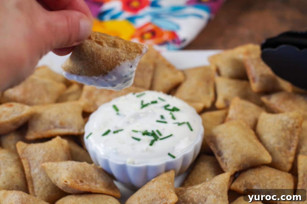 Crispy Air Fryer Pizza Bite being dipped into creamy sauce, with a tray of more golden pizza bites in the background.