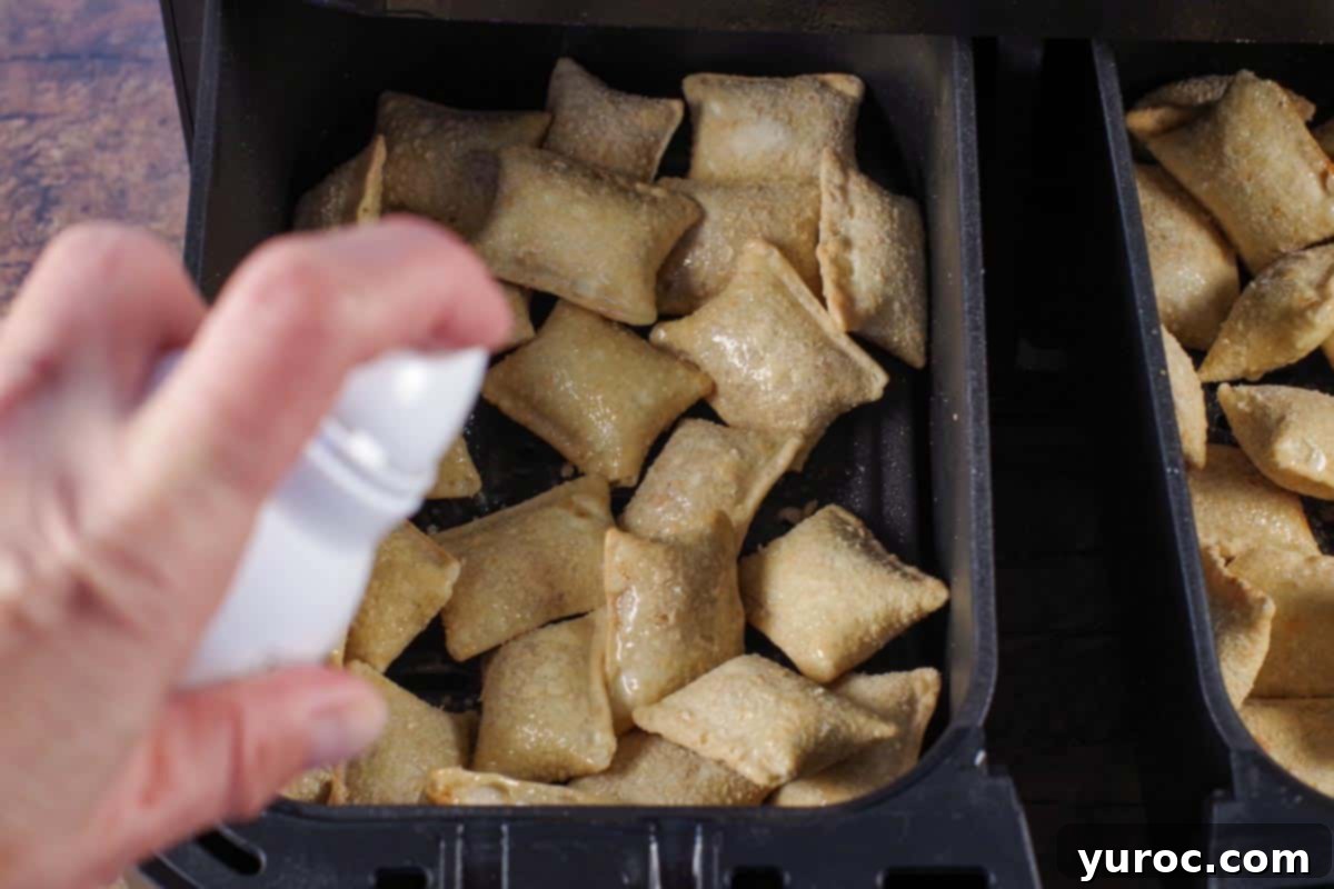 Frozen pizza bites generously sprayed with cooking oil inside an air fryer basket before cooking.