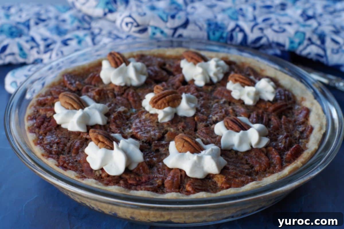 pecan pie in glass pie dish, on blue surface, with blue patterned oven mitts in the background
