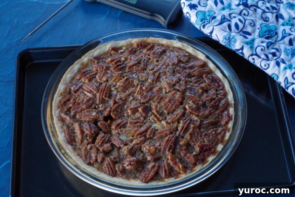 baked pecan pie on black baking sheet with blue patterned oven mitts