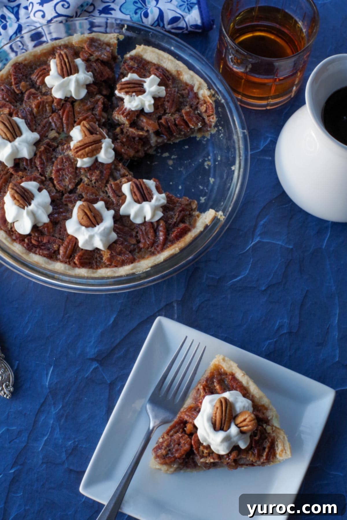 piece of Maple Pecan Pie on a white plate with fork and whole pie with piece missing, as well as maple syrup and glass of bourbon