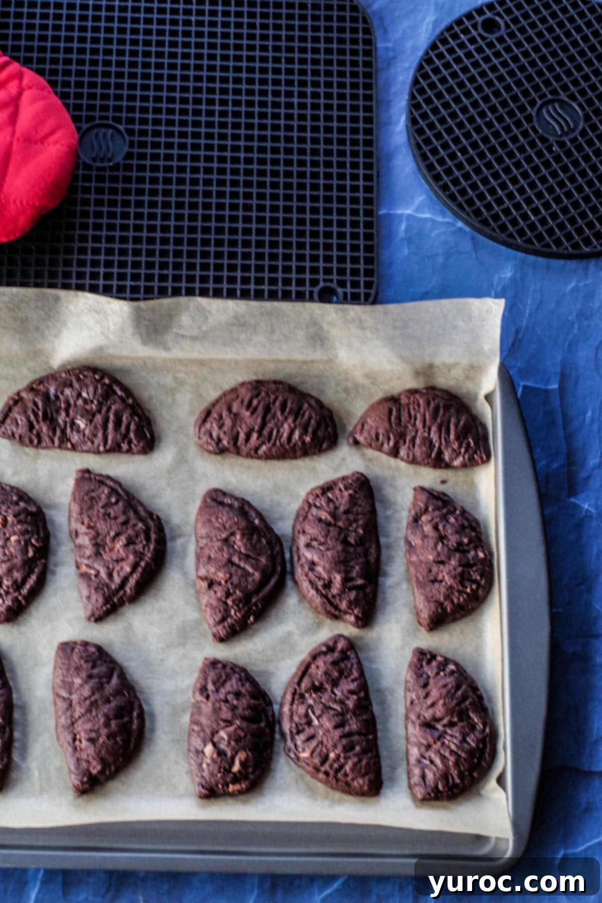 chocolate orange cookies on a parchment covered pan with round and rectangular silicone trivets in the background