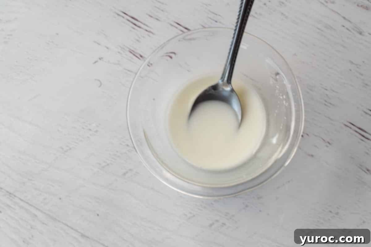 A small glass bowl containing cornstarch mixed with cold water, forming a slurry ready to thicken the sauce.