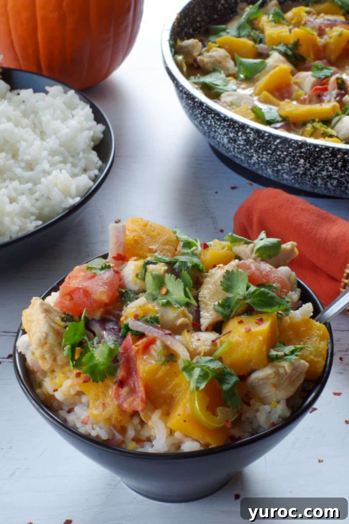 A generously filled bowl of Coconut Pumpkin Chicken and jasmine rice, placed next to a larger serving dish of the chicken curry, creating an inviting culinary scene.