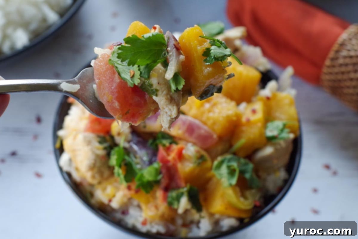 A close-up shot of a tender piece of pumpkin and chicken, held delicately on a fork, hovering above a bowl filled with more of the appetizing Coconut Pumpkin Chicken curry.