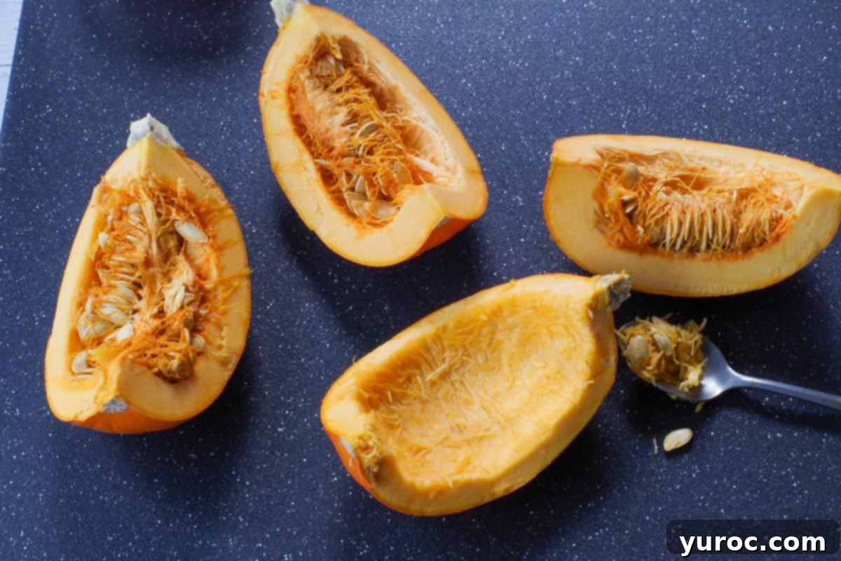 A sugar pumpkin cut into quarters, with the stringy pulp and seeds being carefully scooped out, ready for preparation.