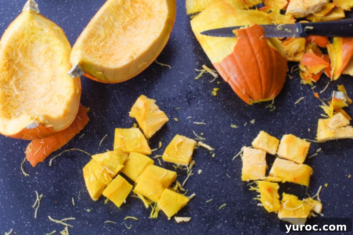 Softened pumpkin being carefully peeled and then cut into uniform, bite-sized pieces on a cutting board.