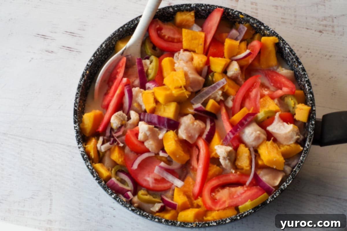 Sliced tomatoes being added to the simmering Coconut Pumpkin Chicken mixture in the frying pan, enhancing its color and flavor.