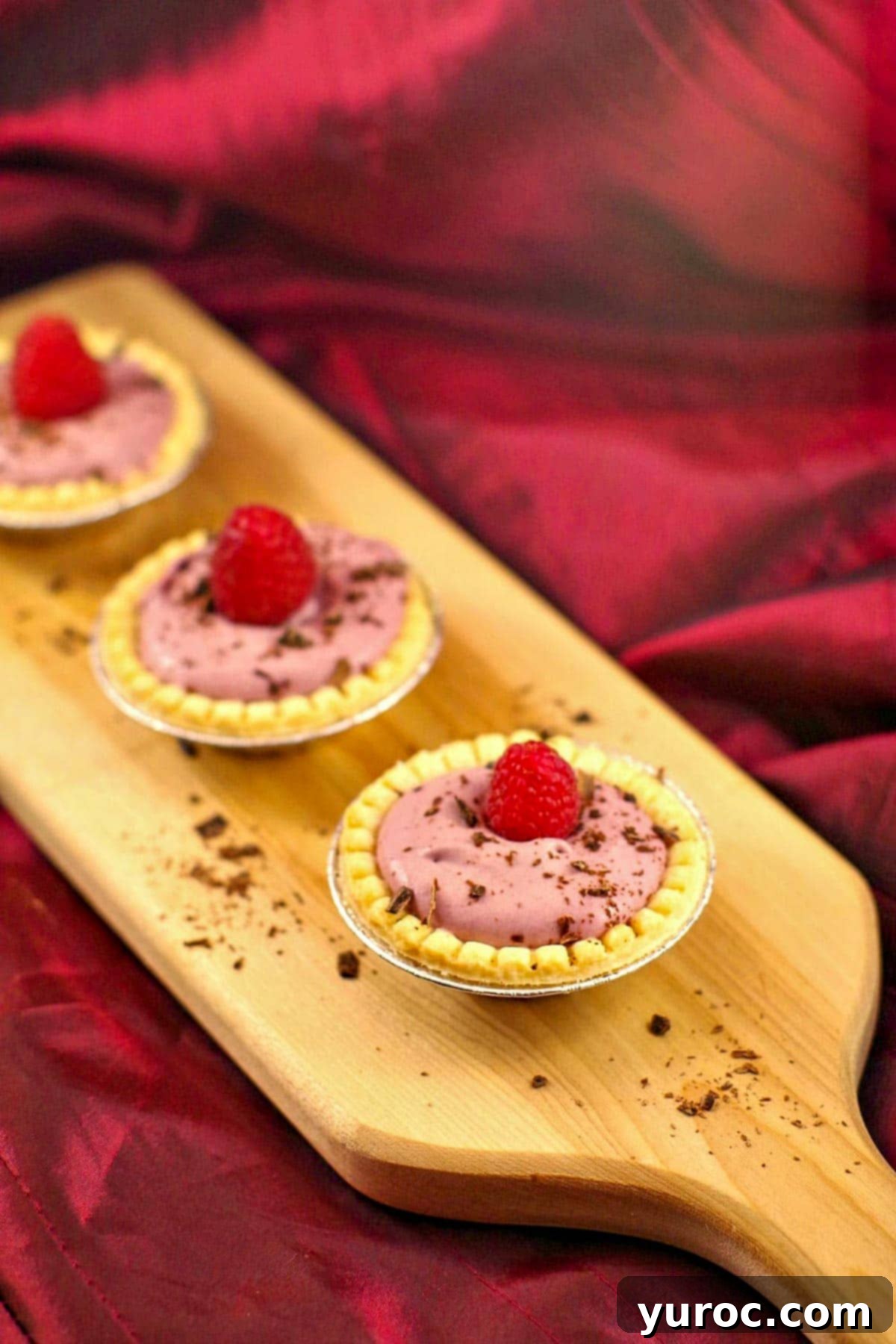 3 raspberry tiramisu tarts on a narrow wooden cutting board
