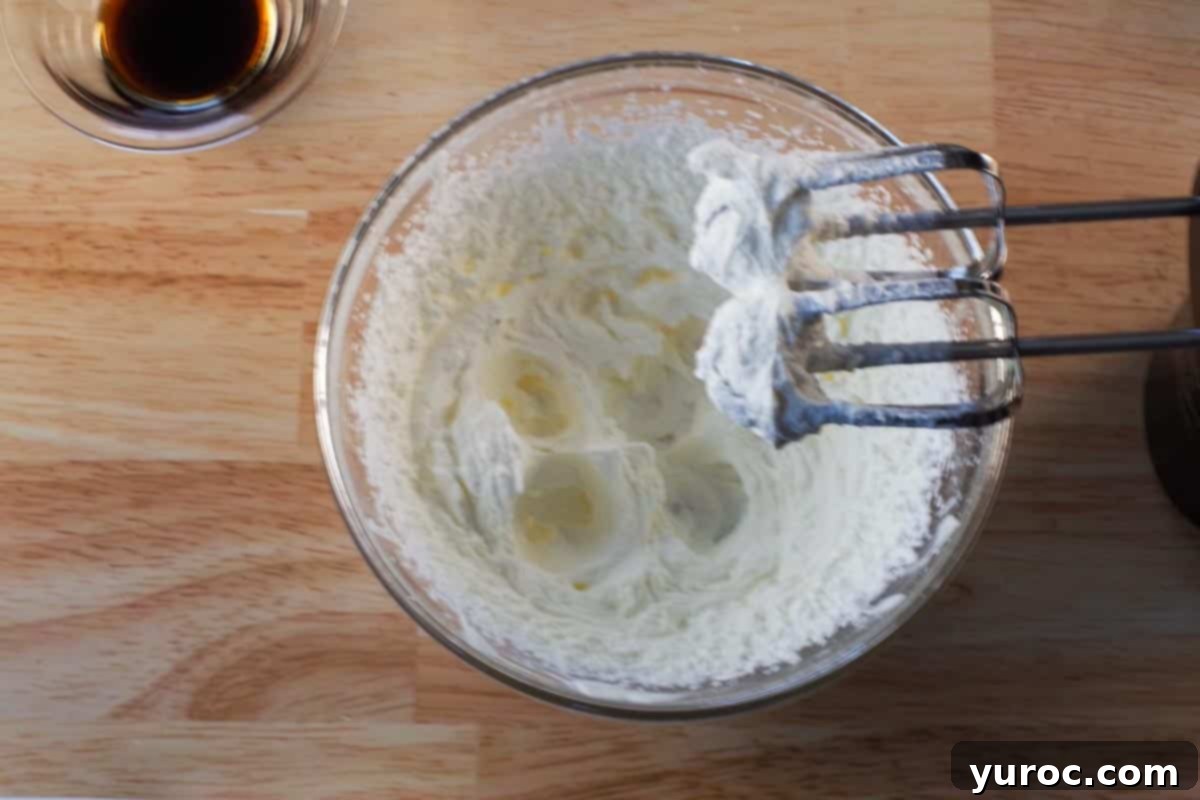 Whipped cream beaten to stiff peaks in glass bowls with beaters above.