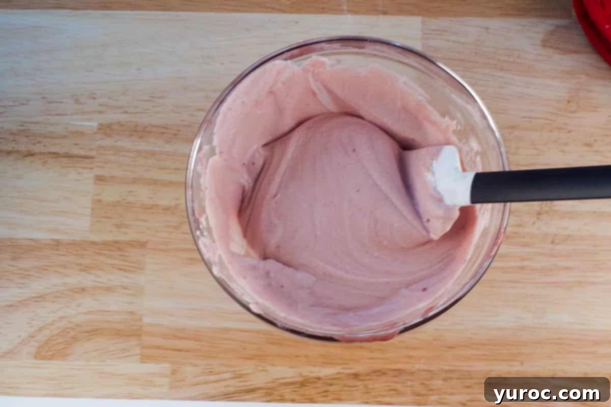 Whipped Cream mixed with mascarpone mixture in glass bowl with spatula. 