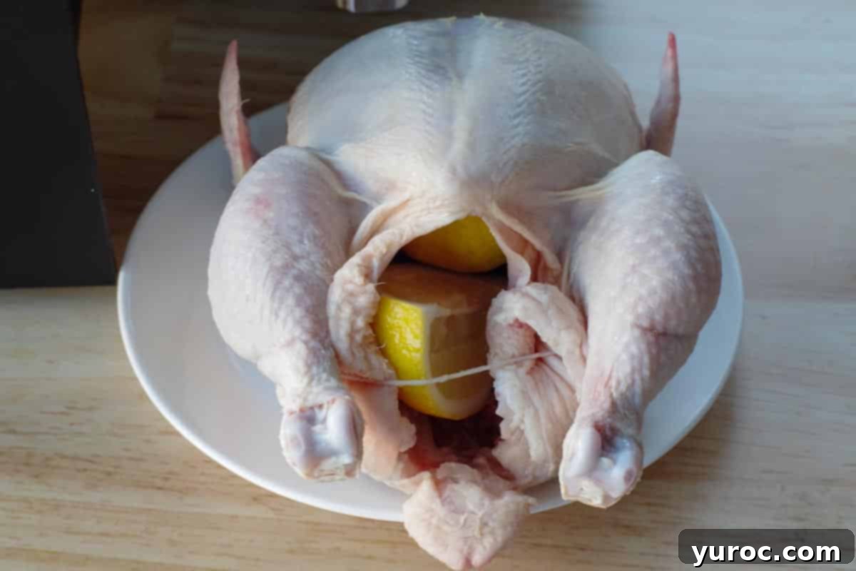 Raw whole chicken on a plate with lemon wedges inserted into its cavity, ready for seasoning.