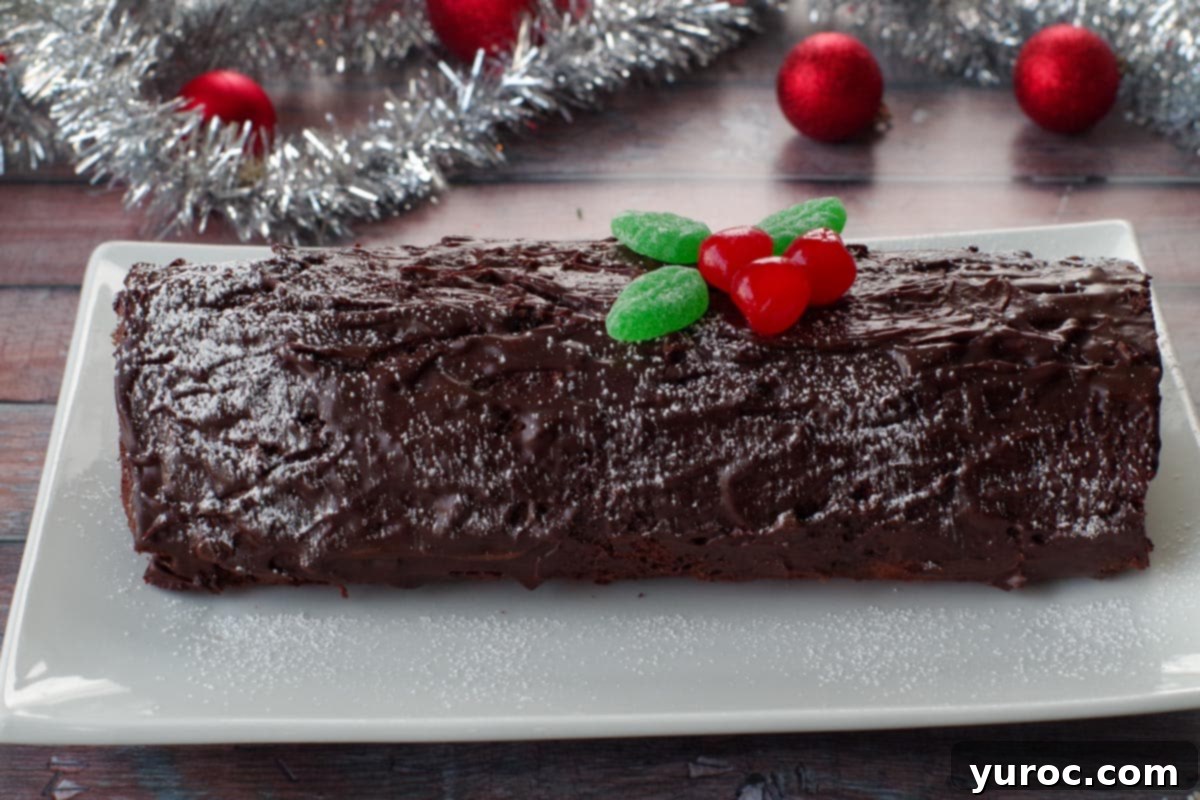 whole black forest yule log cake on a white platter with tinsel and red tree decorations in background