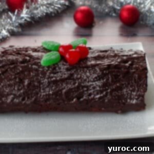 whole black forest yule log cake on a white platter with tinsel and red tree decorations in background