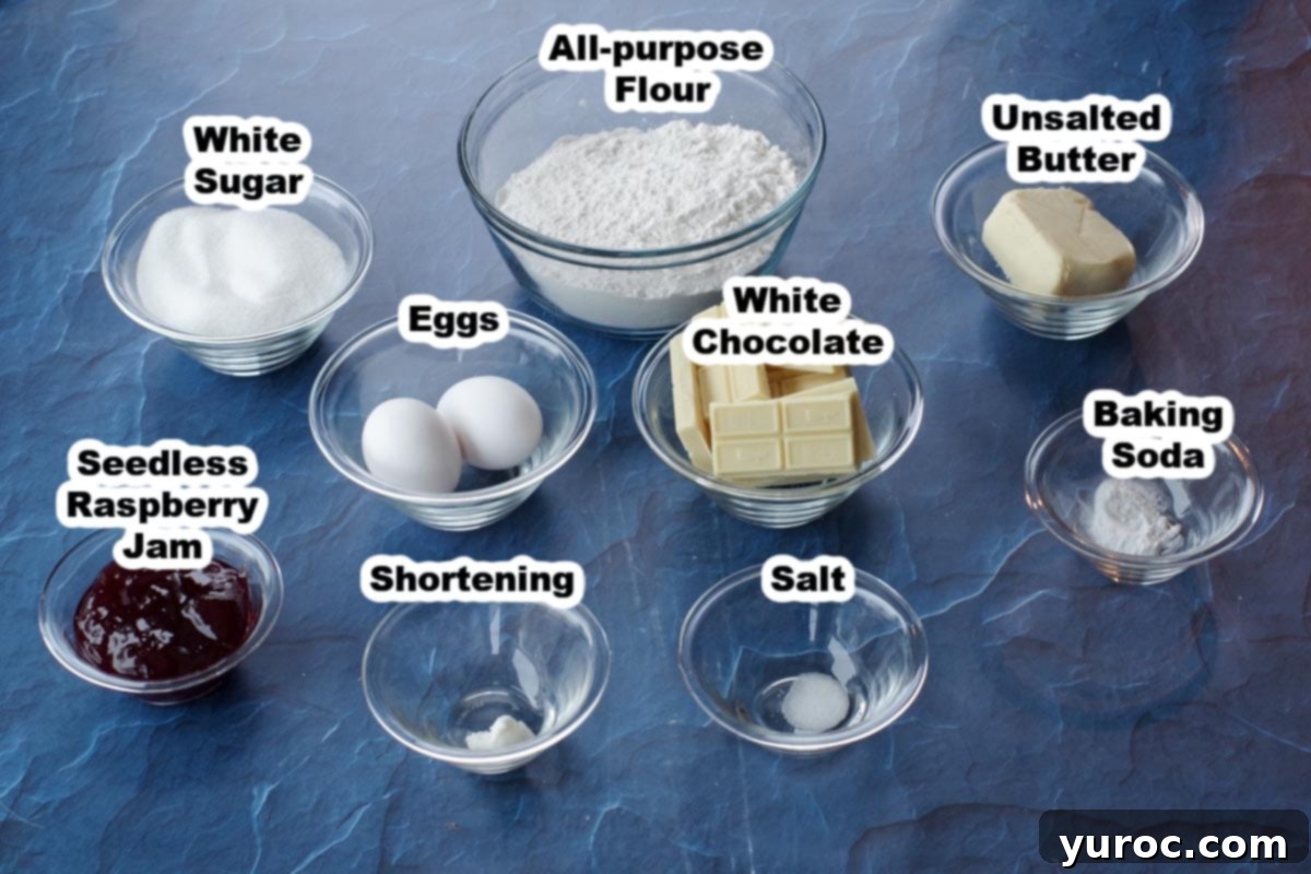 ingredients for white chocolate raspberry cookies in glass jars, labelled, on blue surface