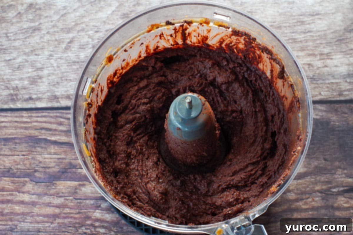 Decadent Dark Chocolate Date Hummus 8 Mini chocolate chips are scattered over the smooth dark chocolate hummus in the food processor bowl, ready for a quick final blend.