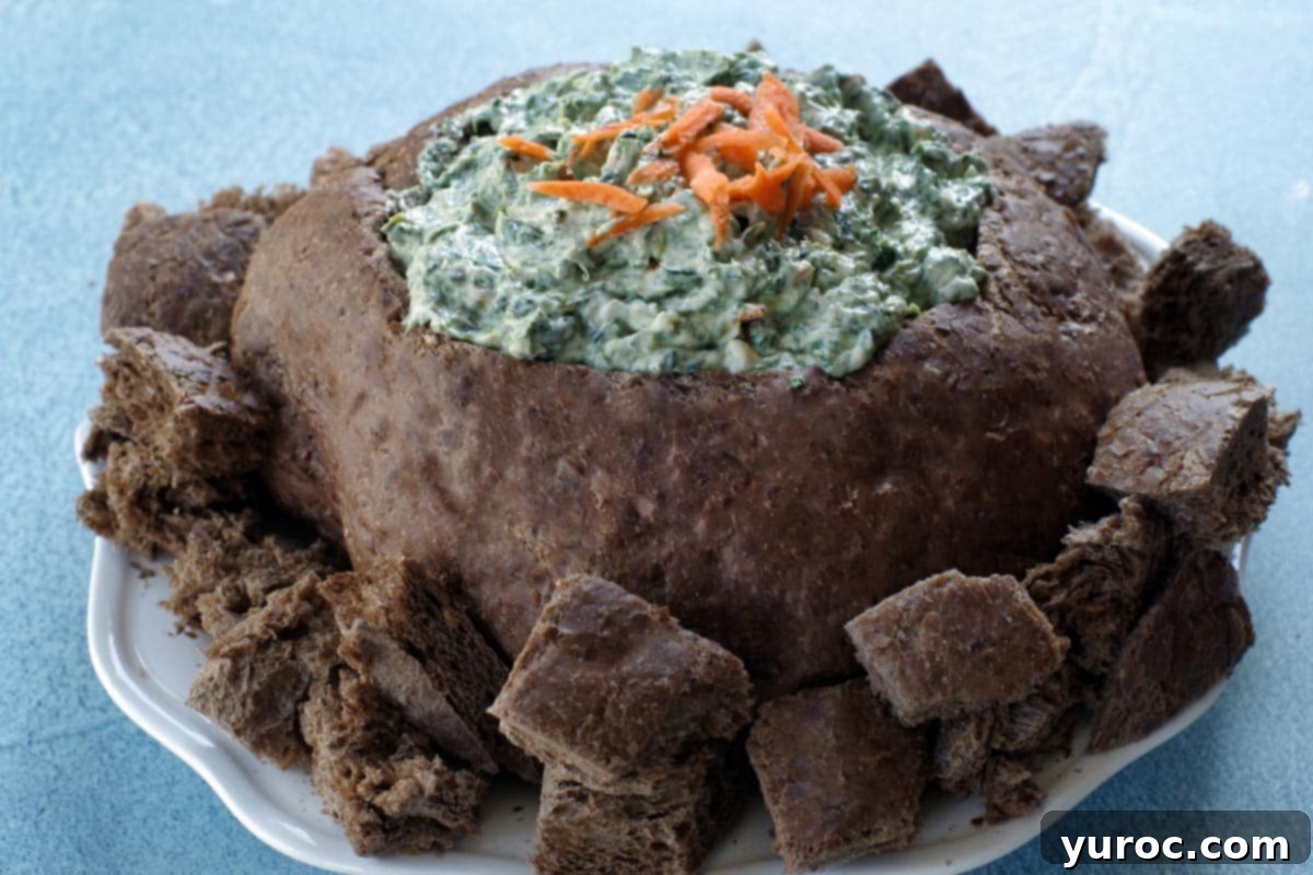Ultimate Pumpernickel Spinach Dip 1 Creamy Pumpernickel Spinach Dip served in an edible bread bowl, surrounded by cubed pumpernickel bread for dipping.