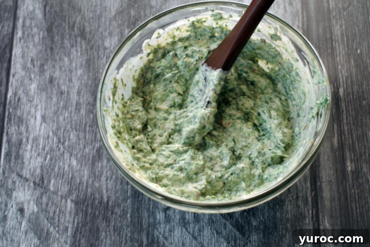 Ultimate Pumpernickel Spinach Dip 4 Pumpernickel spinach dip ingredients being thoroughly mixed together in a glass bowl with a wooden spoon.