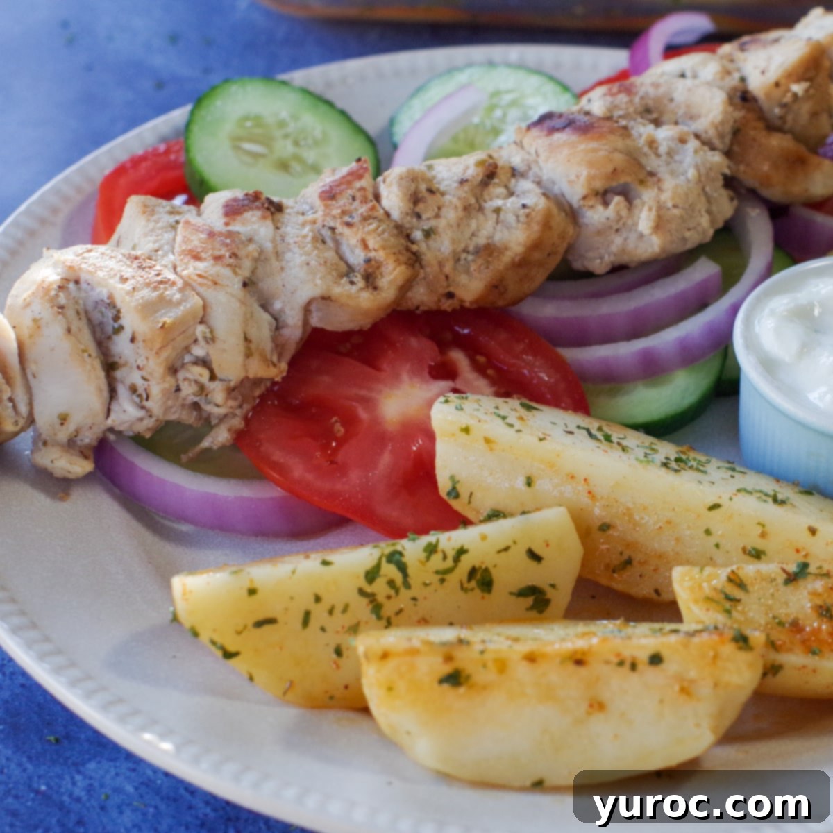 Greek chicken souvlaki on a bed of veggies with greek potatoes, lemon and tzatziki sauce